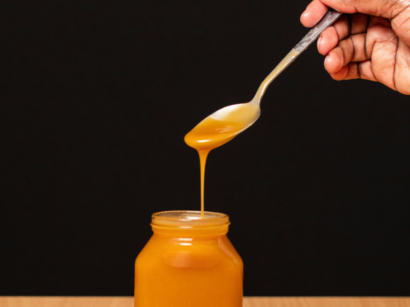 Crystallized honey in a jar with spoon showing sugar crystals under warm natural light.