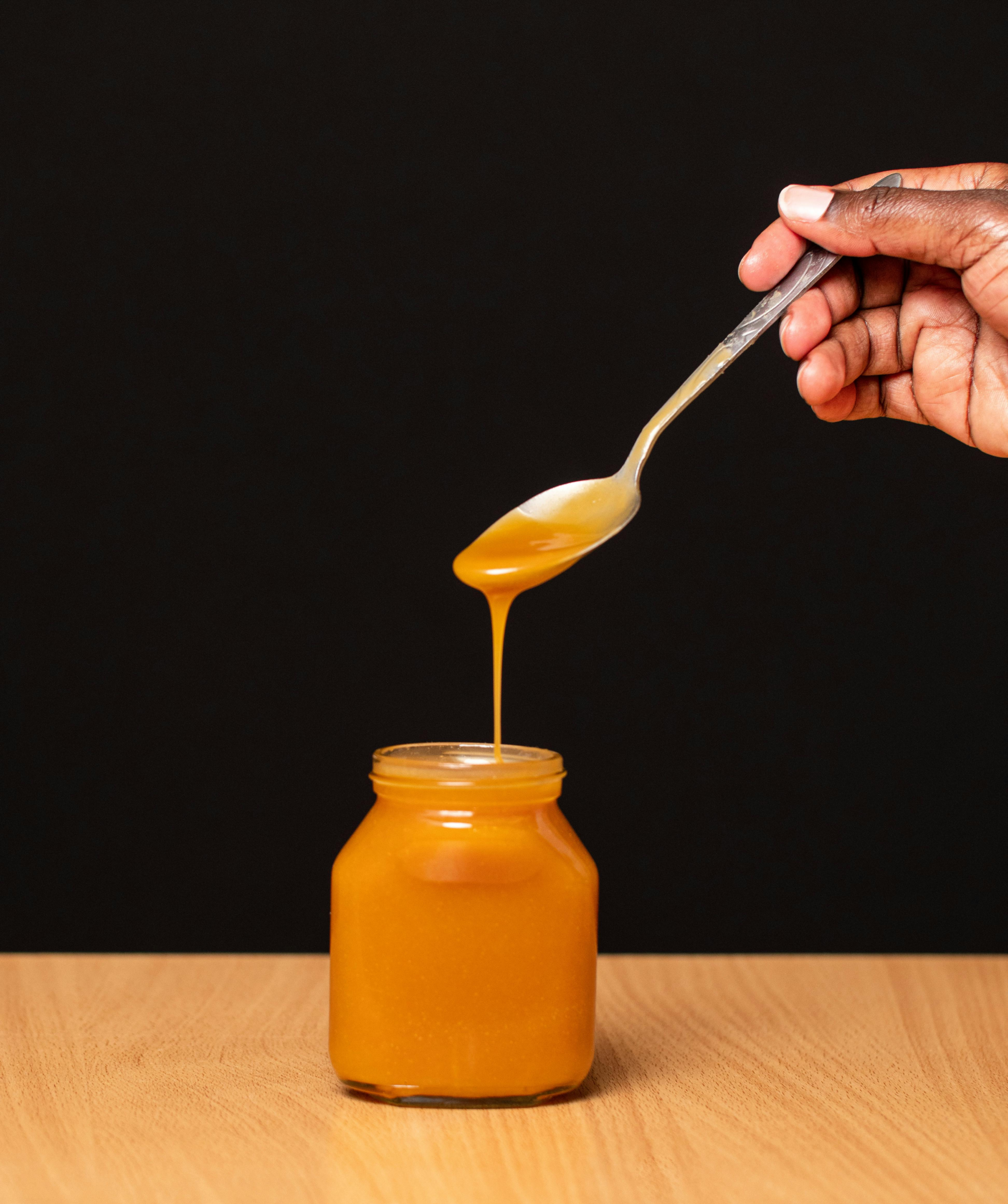 Crystallized honey in a jar with spoon showing sugar crystals under warm natural light.