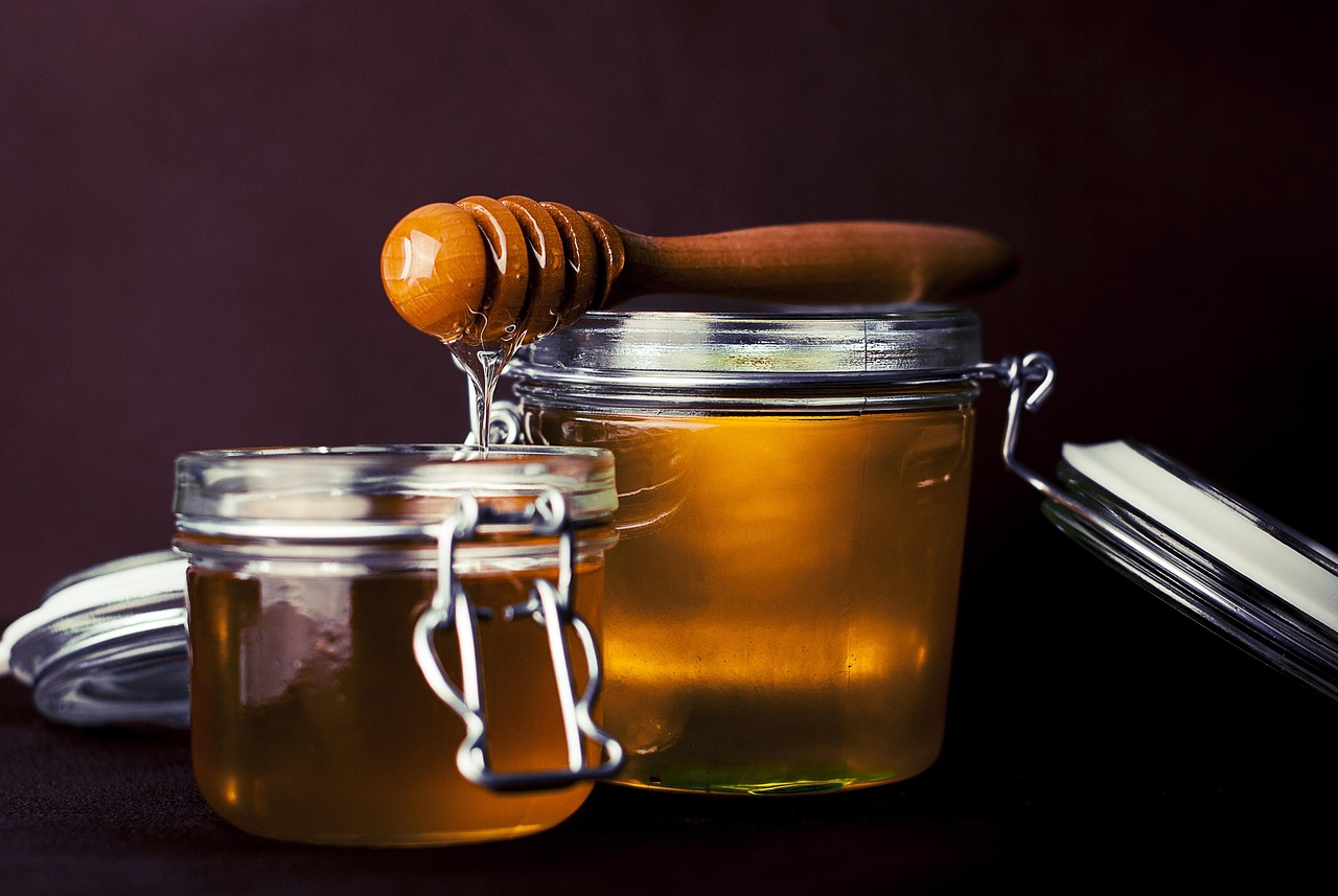 jar of golden honey with honey dipper and honeycomb
